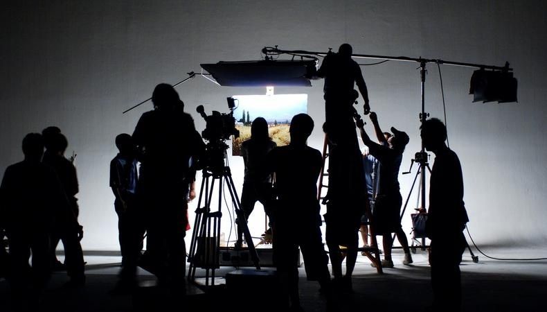 Filmteam i siluett arbetar med kamera och ljusutrustning i en studio